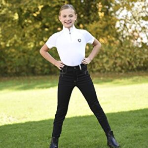 Covalliero Kinder Basic Plus Reithose, Schwarz, 164 EU - Eine hübsche junge Mädchen steht auf einer grünen Wiese mit ihren Händen auf den Hüften. Sie trägt ein weißes Poloshirt, schwarze Hose und schwarze Stiefel.